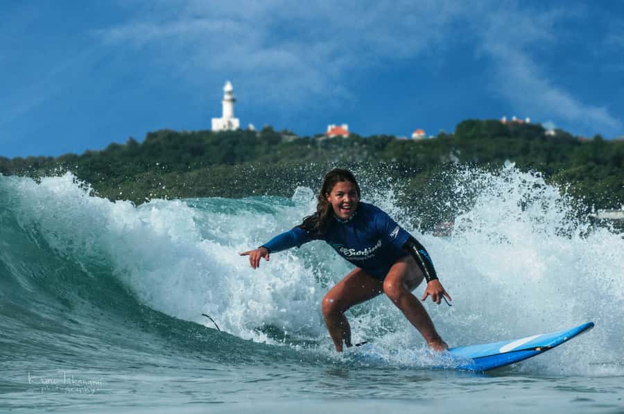 A surfer carving a wave below the lighthouse at Byron Bay